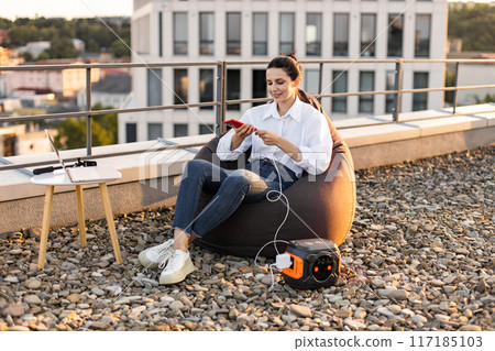 Businesswoman relaxing on rooftop with portable power station 117185103