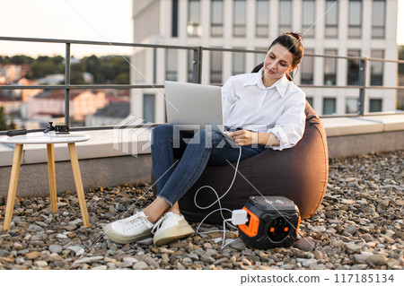 Business woman charging laptop with portable power station on rooftop 117185134