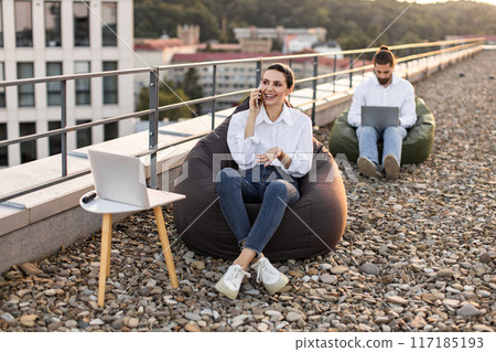 Two people working remotely on rooftop with laptops and bean bags 117185193