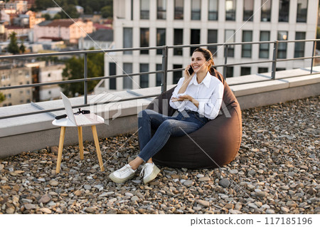 Woman working on rooftop using laptop and phone 117185196