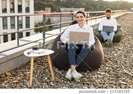 Business people working outdoors on rooftop with laptops 117185285