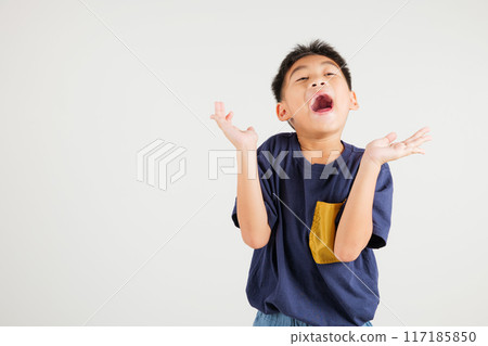 A jubilant kid boy raises her fists in celebration of her success, saying yes with excitement. Asian portrait of a happy young primary child in a studio shot on a white background, winning 117185850
