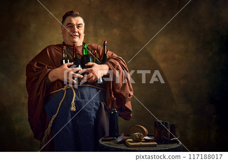 Delightful man, monk holding various bottles filled with beer, ale, and wine against vintage background. Rich heritage of monastic brewing. 117188017