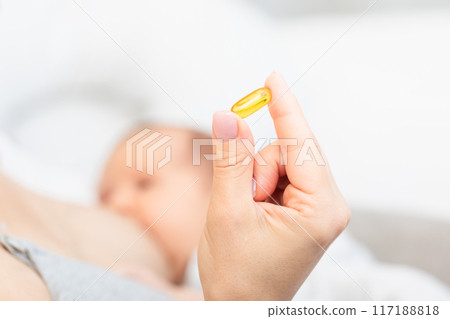 Hand Holding Yellow Pill with Breastfeeding Baby in Background Hand Holding Yellow Pill with Breastfeeding Baby in Background 117188818