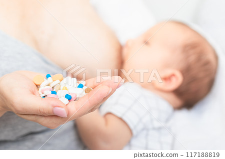 Mother holding heap of pills while breastfeeding newborn baby 117188819