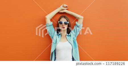 Portrait of modern stylish young woman in white glasses, casual clothing posing on orange background Portrait of modern stylish young woman in white glasses, casual clothing posing on orange background 117189226