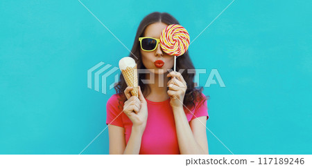 Summer portrait happy young woman holding ice cream cone, lollipop blowing kiss on blue background Summer portrait happy young woman holding ice cream cone, lollipop blowing kiss on blue background 117189246