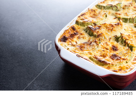 Casserole with cheese and gratin zucchini on black slate background Casserole with cheese and gratin zucchini on black slate background 117189485