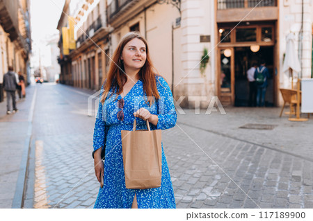 Happy 30s woman holding paper shopping bag on old town background. Zero waste concept. Eco Nature Friendly Style. Environmental Conservation Recycling mock up Happy 30s woman holding paper shopping bag on old town background. Zero waste concept. Eco Nature Friendly Style. Environmental Conservation Recycling mock up 117189900