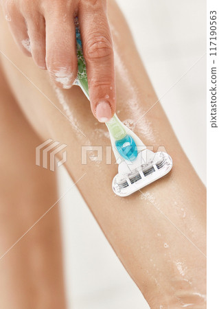 Young woman shaving her legs with razor in white shower, close-up Young woman shaving her legs with razor in white shower, close-up 117190563