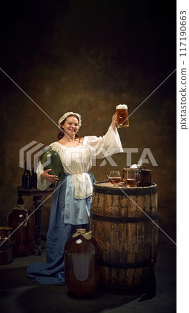 Woman brewer, dressed old-fashion clothes, holding high fresh-cooked, frothy glass of beer at ancient pub against vintage background. 117190663
