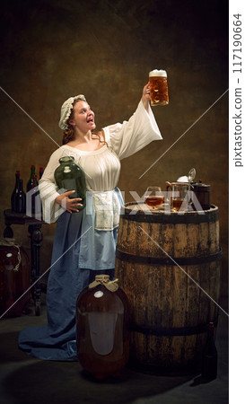 Woman brewer, dressed old-fashion clothes, holding high fresh-cooked, frothy glass of beer at ancient pub against vintage background. Woman brewer, dressed old-fashion clothes, holding high fresh-cooked, frothy glass of beer at ancient pub against vintage background. 117190664