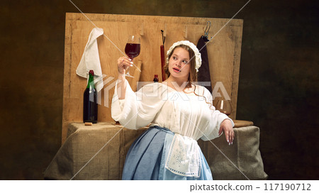 Young chubby medieval woman in vintage clothes holding glass of wine standing at ancient bar counter and enjoy evening. 117190712