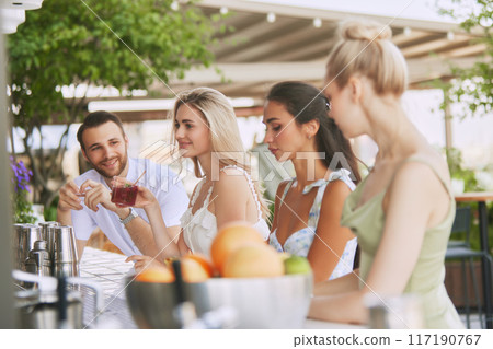Friends, man and beautiful young women enjoying cocktails and friendly atmosphere at chic outdoor bar. Weekend vibes 117190767