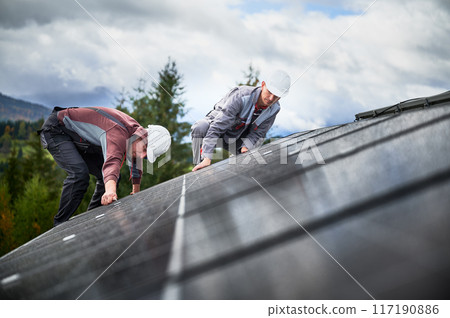 Mounters installing photovoltaic solar panels on roof of house. Men engineers in helmets building solar module system with help of hex key. Concept of alternative, renewable energy. Mounters installing photovoltaic solar panels on roof of house. Men engineers in helmets building solar module system with help of hex key. Concept of alternative, renewable energy. 117190886