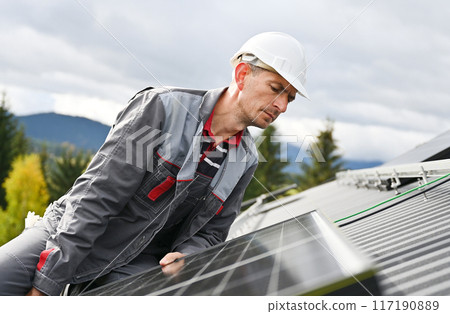 Man builder mounting photovoltaic solar moduls on roof of house. Close up engineer in helmet looking on evenness of solar panel during installing. Concept of alternative and renewable energy. 117190889