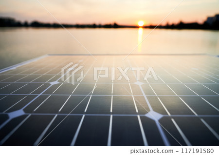 Solar panel with sun setting over calm lake in background. Peaceful ambiance of renewable energy technology in harmony with nature, highlighting sustainability and innovation. Solar panel with sun setting over calm lake in background. Peaceful ambiance of renewable energy technology in harmony with nature, highlighting sustainability and innovation. 117191580