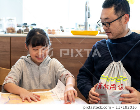 A daughter checking the location of her house on a hazard map while her father looks on, carrying an emergency kit 117192016