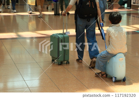 Parent and child heading to the international counter; child being pulled straddling a carry-on bag 117192320