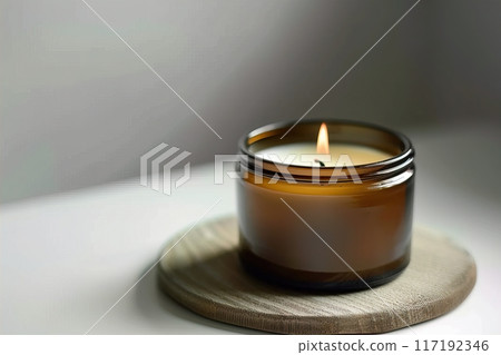 A cozy aromatherapy candle in a brown glass jar on wooden base creates a warm and tranquil ambiance 117192346