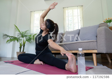 Young Woman Practicing Yoga at Home in a Cozy Living Room Setting with Natural Light and Comfortable Furniture Young Woman Practicing Yoga at Home in a Cozy Living Room Setting with Natural Light and Comfortable Furniture 117192386