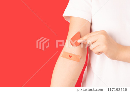 Blood donation. Human hands holding blood drop shape with plaster heart on arm against red background. Hematologic disorders such as anemia, sickle cell disease, hemophilia, leukemia and ITP. 117192516