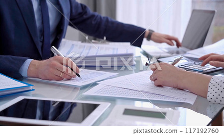 Business colleagues accountants or auditors reviewing financial data in office. Two professionals analyzing paper reports and using calculators. Audit and taxes Business colleagues accountants or auditors reviewing financial data in office. Two professionals analyzing paper reports and using calculators. Audit and taxes 117192760
