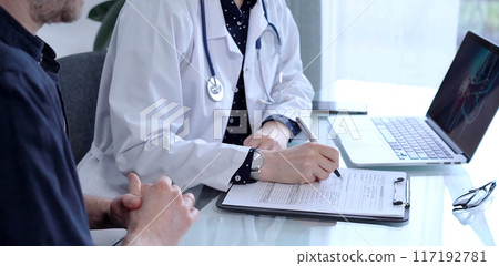 Doctor and patient are talking in clinic after usual health check up. Female physician is making notes awhile man is describing something. Medicine concept Doctor and patient are talking in clinic after usual health check up. Female physician is making notes awhile man is describing something. Medicine concept 117192781