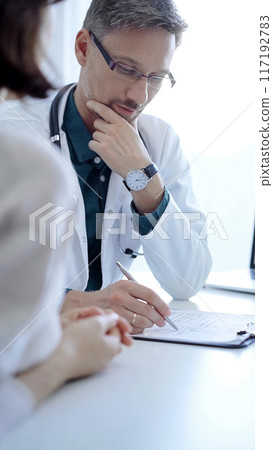 Doctor and a patient. The physician, wearing a white medical coat over a green shirt, gesturing with his hands during a consultation in the clinic. Medicine concept 117192783