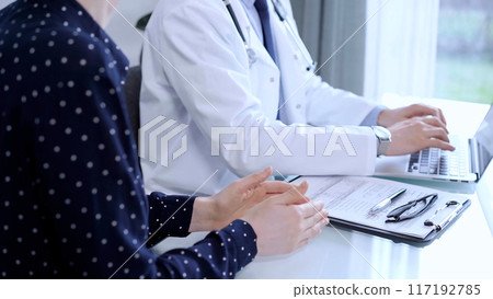 Doctor and patient are talking in clinic after health exam. Male physician is using laptop and discussing test results with a senior woman. Medicine concept 117192785