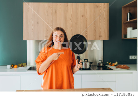 Young woman housewife holding empty pan in the kitchen at home. Domestic life and diet concept. Food banner. Time to eat 117193053