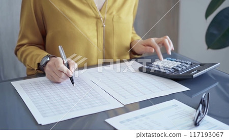 Professional business woman in yellow blouse is working on financial reports. Close-up of a woman's hands using calculator for audit or accounting Professional business woman in yellow blouse is working on financial reports. Close-up of a woman's hands using calculator for audit or accounting 117193067