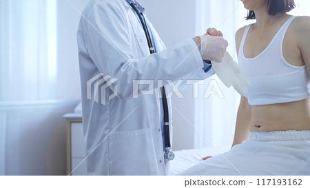 Doctor and patient. Physician putting white medical gloves is ready to examine female patient in clinic. Orthopedics and medicine 117193162