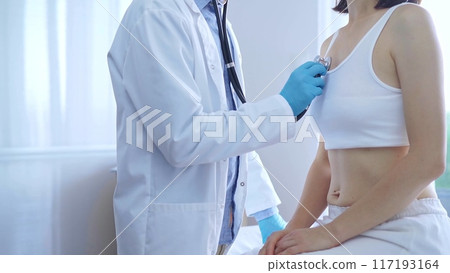 Doctor and patient. Physician wearing blue medical gloves is using stethoscope examining woman lungs in clinic. Medicine concept 117193164