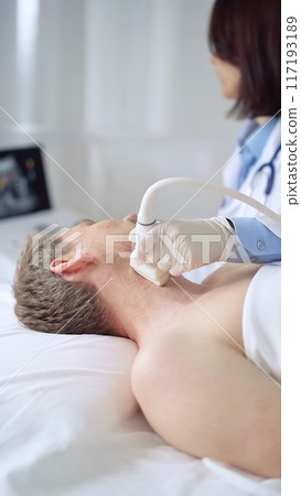 Doctor performing neck ultrasound exam on male patient 117193189