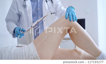 Doctor man wearing blue medical gloves examines a patient's knee during a medical consultation in a clinic. The concept of medicine and orthopedics 117193277
