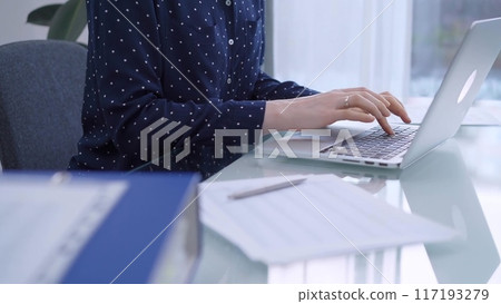 A female accountant or businesswoman with blue dotted blousy is typing on laptop computer on glass desk in the office. Business people concept A female accountant or businesswoman with blue dotted blousy is typing on laptop computer on glass desk in the office. Business people concept 117193279