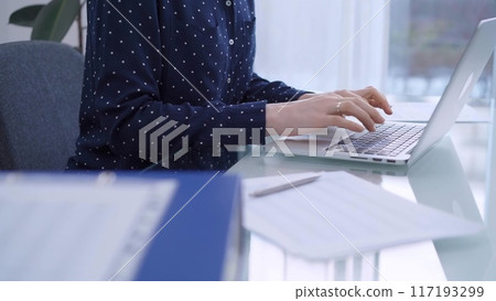 A female accountant or businesswoman with blue dotted blousy is typing on laptop computer on glass desk in the office. Business people concept A female accountant or businesswoman with blue dotted blousy is typing on laptop computer on glass desk in the office. Business people concept 117193299