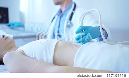 Doctor man wearing a blue medical gloves using an ultrasound equipment on a female patient lying down in clinic cabinet. Medicine concept 117193336