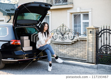 Young business woman sitting in the car, coming home by car. The girl is sitting in the car and holding a mobile phone. Concept of buying goods online and delivering them home 117193467