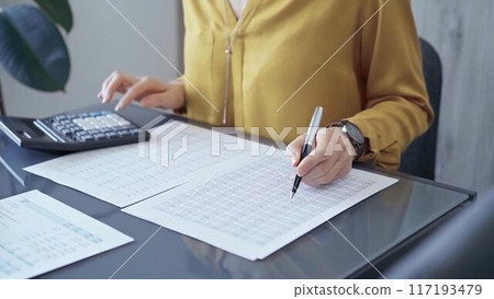 Professional business woman in yellow blouse is working on financial reports. Close-up of a woman's hands using calculator for audit or accounting Professional business woman in yellow blouse is working on financial reports. Close-up of a woman's hands using calculator for audit or accounting 117193479