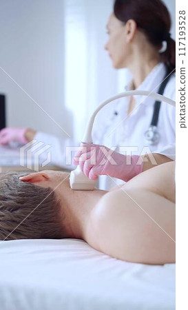 Doctor woman with pink medical gloves performing neck ultrasound exam on male patient. Thyroid gland examination. Medicine concept Doctor woman with pink medical gloves performing neck ultrasound exam on male patient. Thyroid gland examination. Medicine concept 117193528