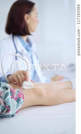 Doctor and kid patient. Orthopedist performing ultrasound examination on a child's knee in a clinic. Medicine and health care 117193569