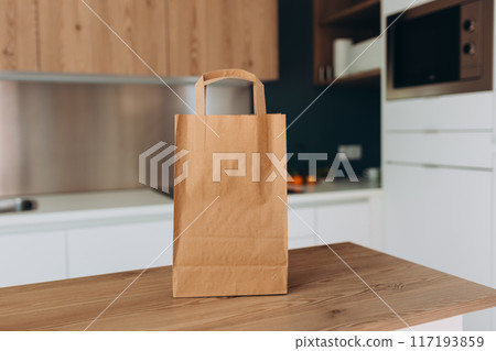 Food craft bag on the wooden table counter in the kitchen. Delivery in any weather around the clock to the client. Fast food eco packaging with big breakfast or diner set Food craft bag on the wooden table counter in the kitchen. Delivery in any weather around the clock to the client. Fast food eco packaging with big breakfast or diner set 117193859