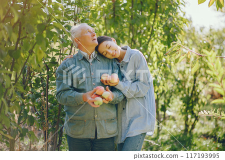 Senior with red apples. Brunette in a blue shirt. Grandfather with grandaughter. Senior with red apples. Brunette in a blue shirt. Grandfather with grandaughter. 117193995