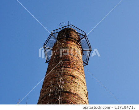 Industrial tower or pipe with observation balcony. Smokestacks with ladder or stairs. Tall brick chimneys above abandoned boiler building for venting smoke, combustion byproducts from factory heating 117194713