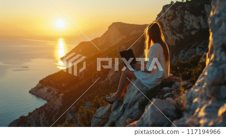 Woman Working on Laptop During Sunset on Rocky Cliff 117194966