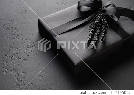 Festive black gift wrapped in paper with ribbon on black surface. Copy space. Close up. Present for Father Day. Black Friday. Festive black gift wrapped in paper with ribbon on black surface. Copy space. Close up. Present for Father Day. Black Friday. 117195002
