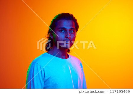 Portrait of young middle Eastern man dressed casually and looking at camera smiling in neon light against gradient orange background. 117195469