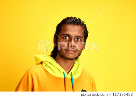 Portrait of young middle Eastern man dressed fashion, vibrant hoodie and looking at camera smiling against yellow studio background. Portrait of young middle Eastern man dressed fashion, vibrant hoodie and looking at camera smiling against yellow studio background. 117195498